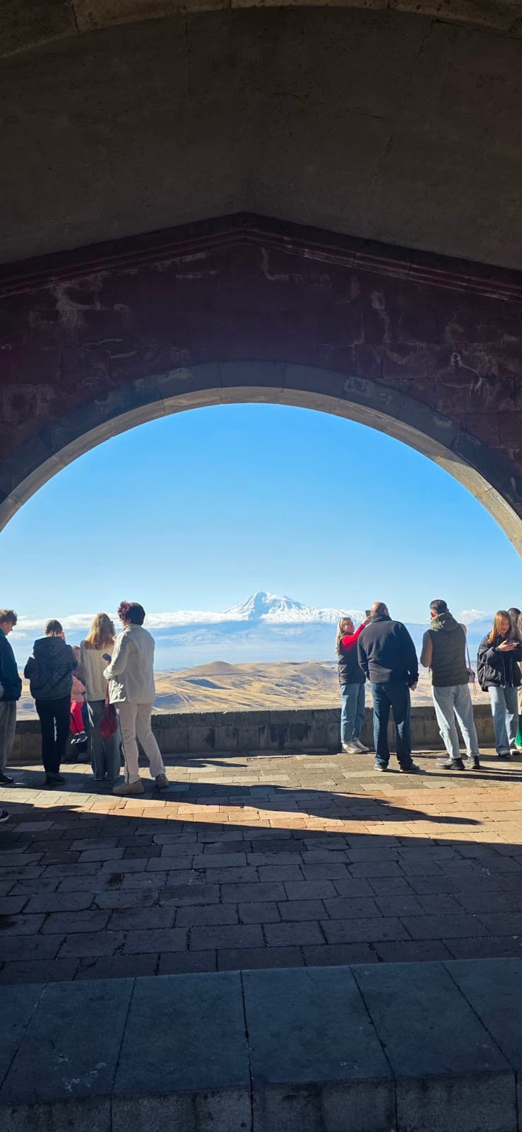 A stone arch framing a distant view of Mount Ararat across the plain