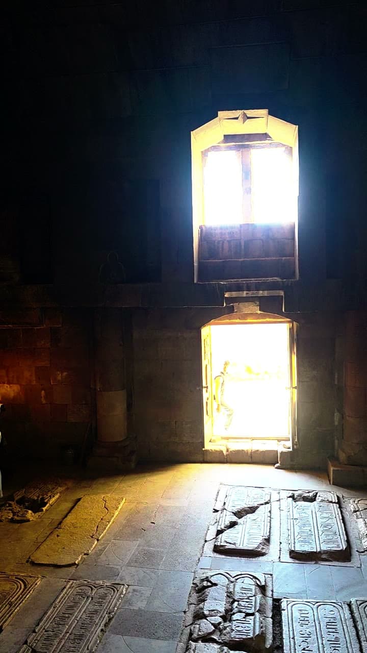 Daylight through a monastery doorway falling across a candlelit stone floor