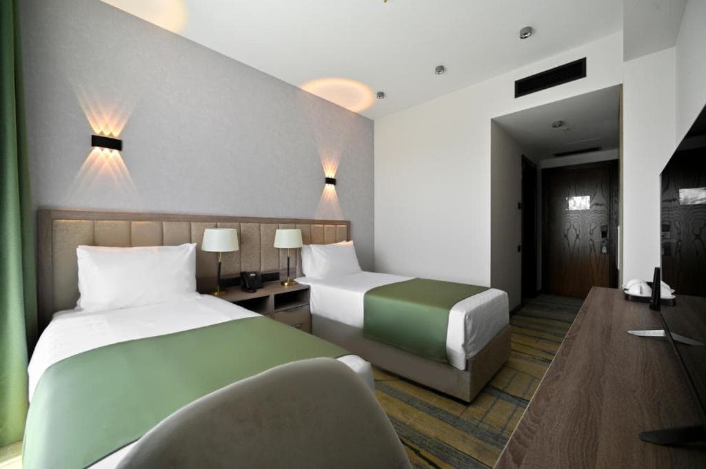 A bright hotel room with two single beds and a vaulted white ceiling