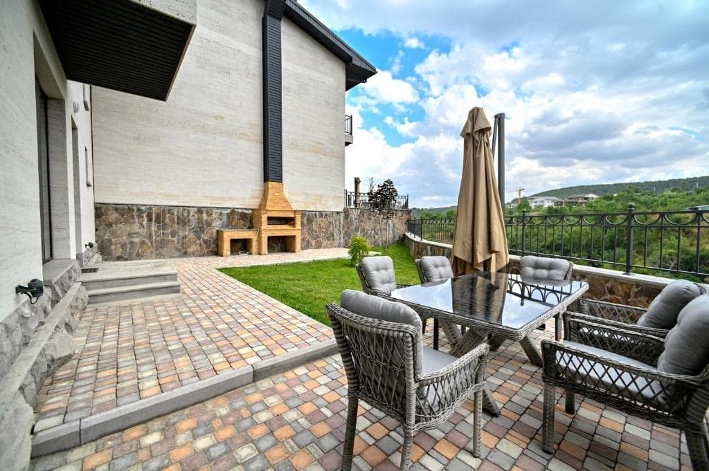A paved outdoor terrace with lounge seating, a parasol and a garden view