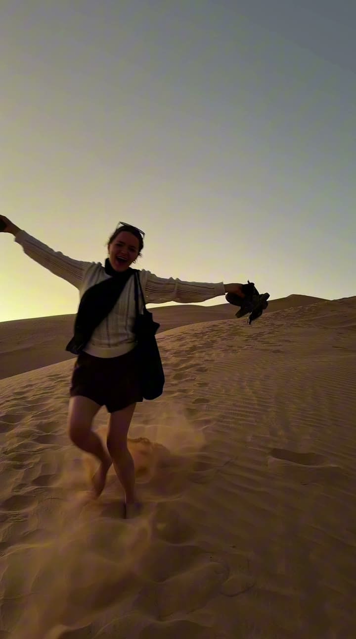 A woman running down a steep dune at sunset with her arms thrown wide