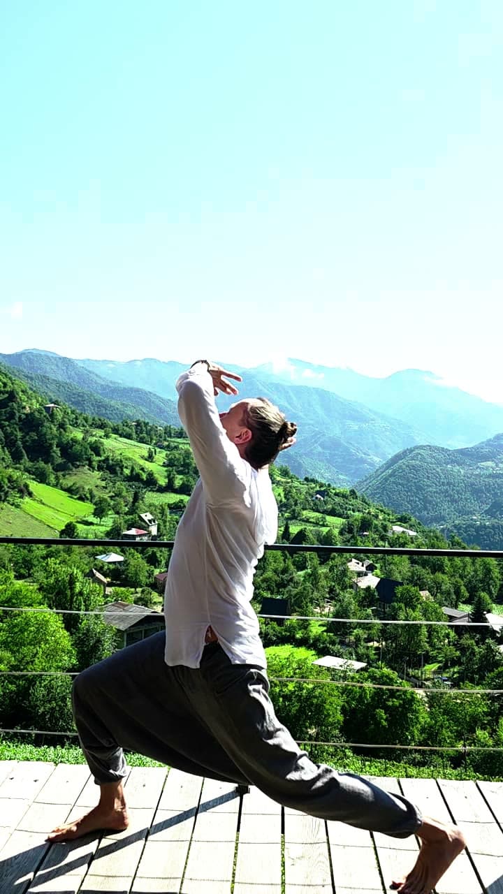 A wide standing qigong posture on a terrace above the valley