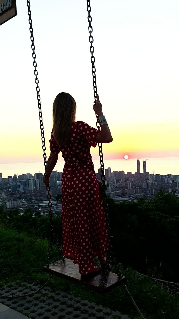 A swing above the city at sunset, the sun low on the horizon