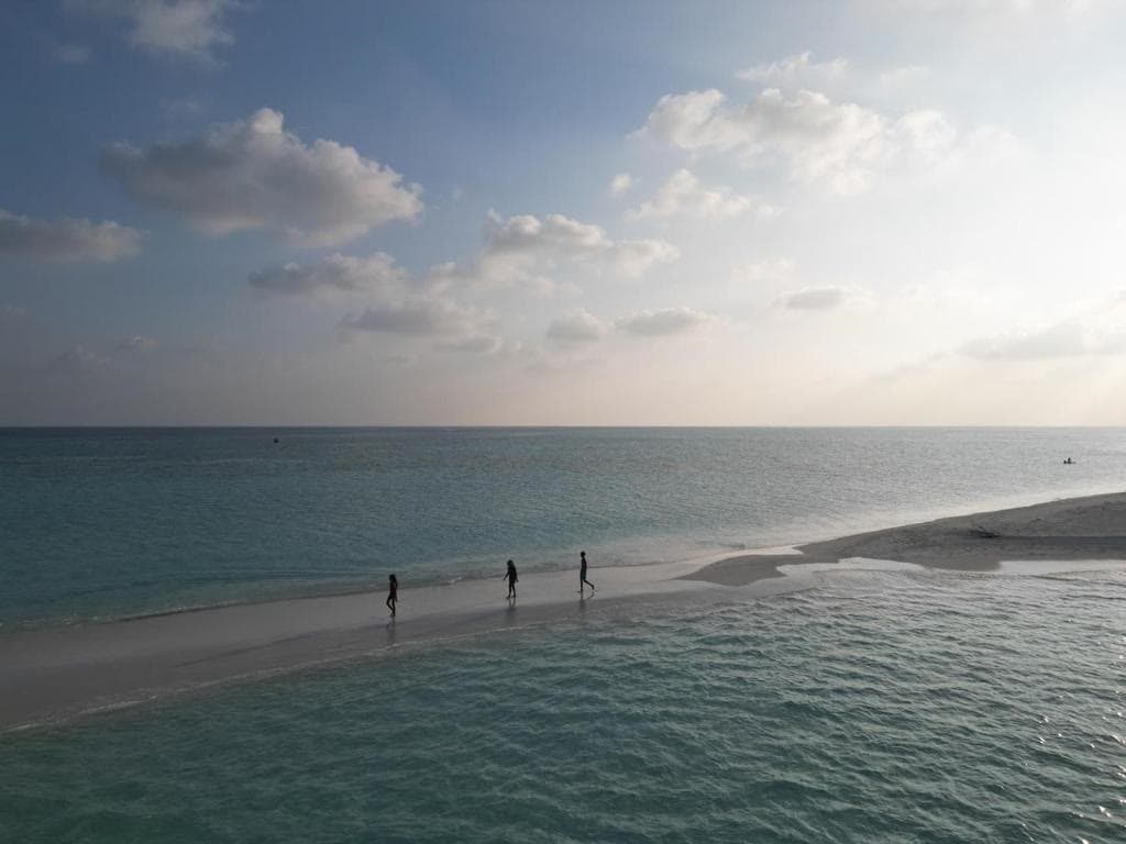 Three figures walking a narrow sandbank at dusk, water on both sides