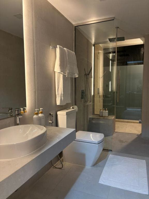 A glass walk-in shower beside a stone vanity with folded towels on a rail