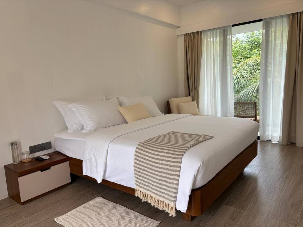 A double bed with a striped throw, beside curtains drawn back from a garden door