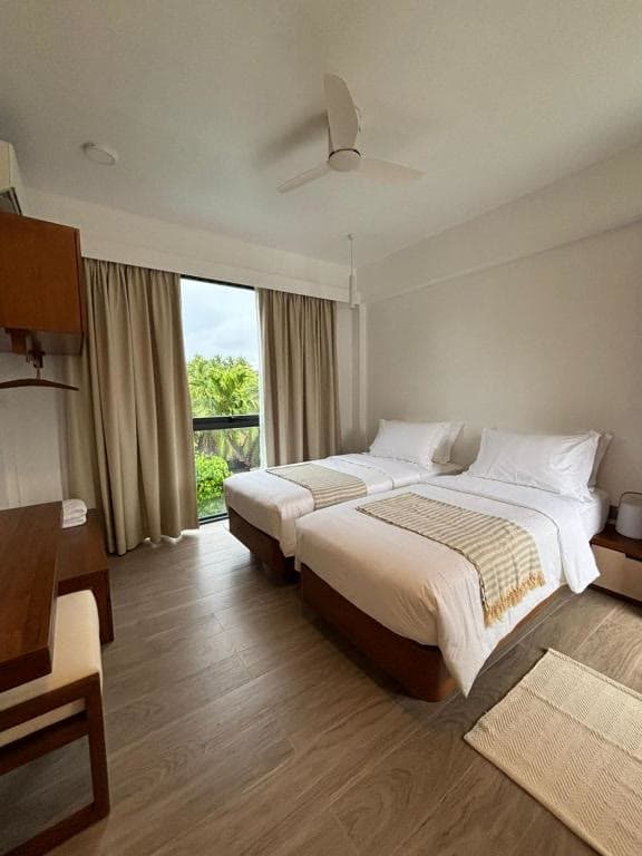A twin room with two low beds, a ceiling fan and a sliding door onto greenery