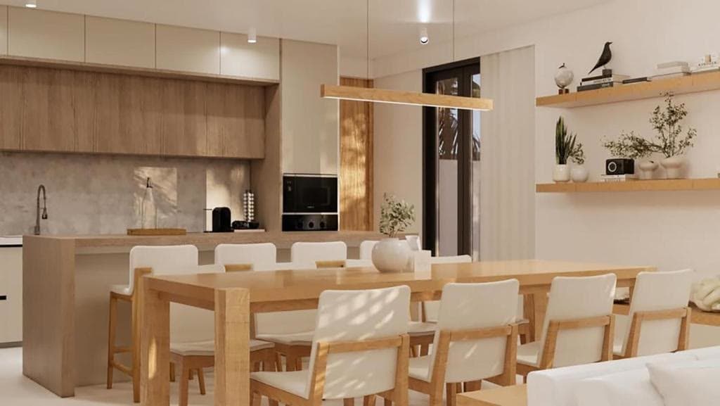An open kitchen in pale wood beside a long dining table set for ten under a linear pendant light