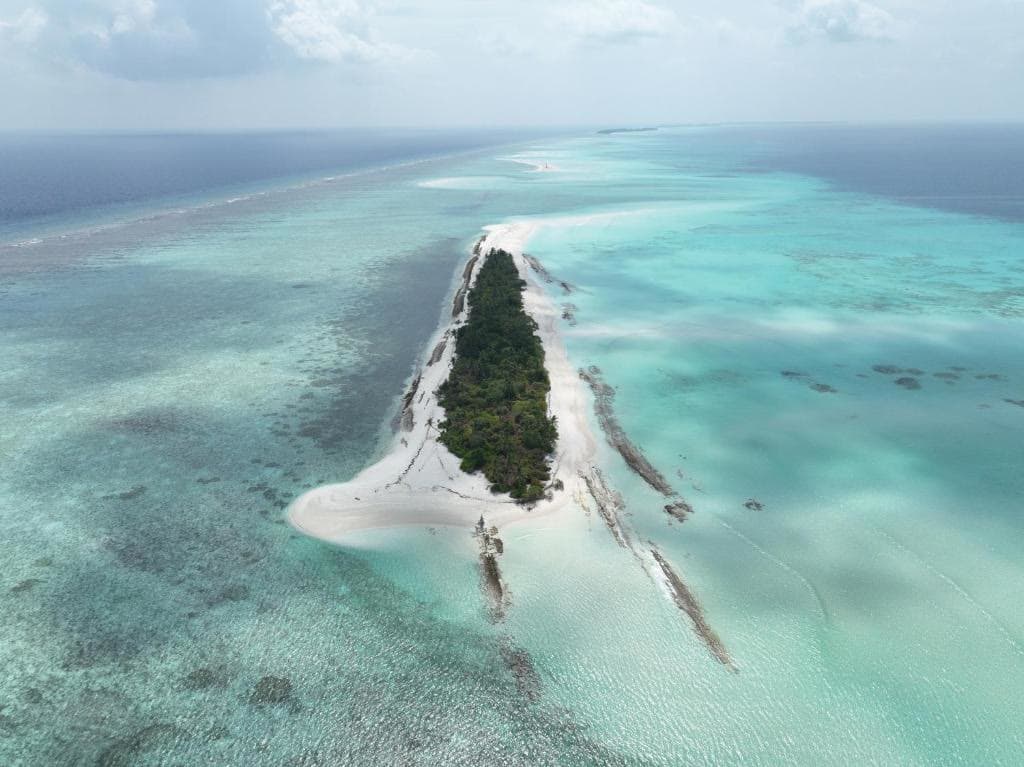 A long uninhabited sand islet lying in pale turquoise reef water