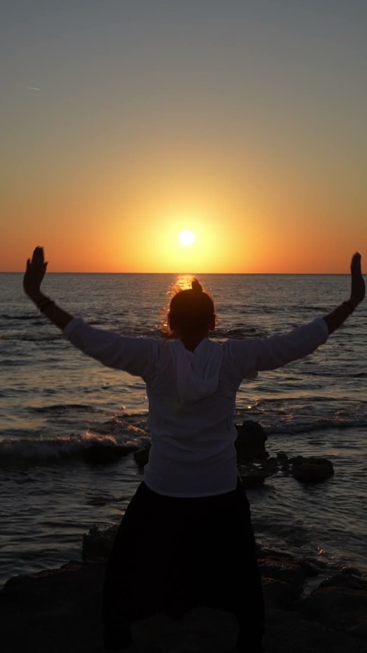 Breath practice with arms raised at sunrise over the sea