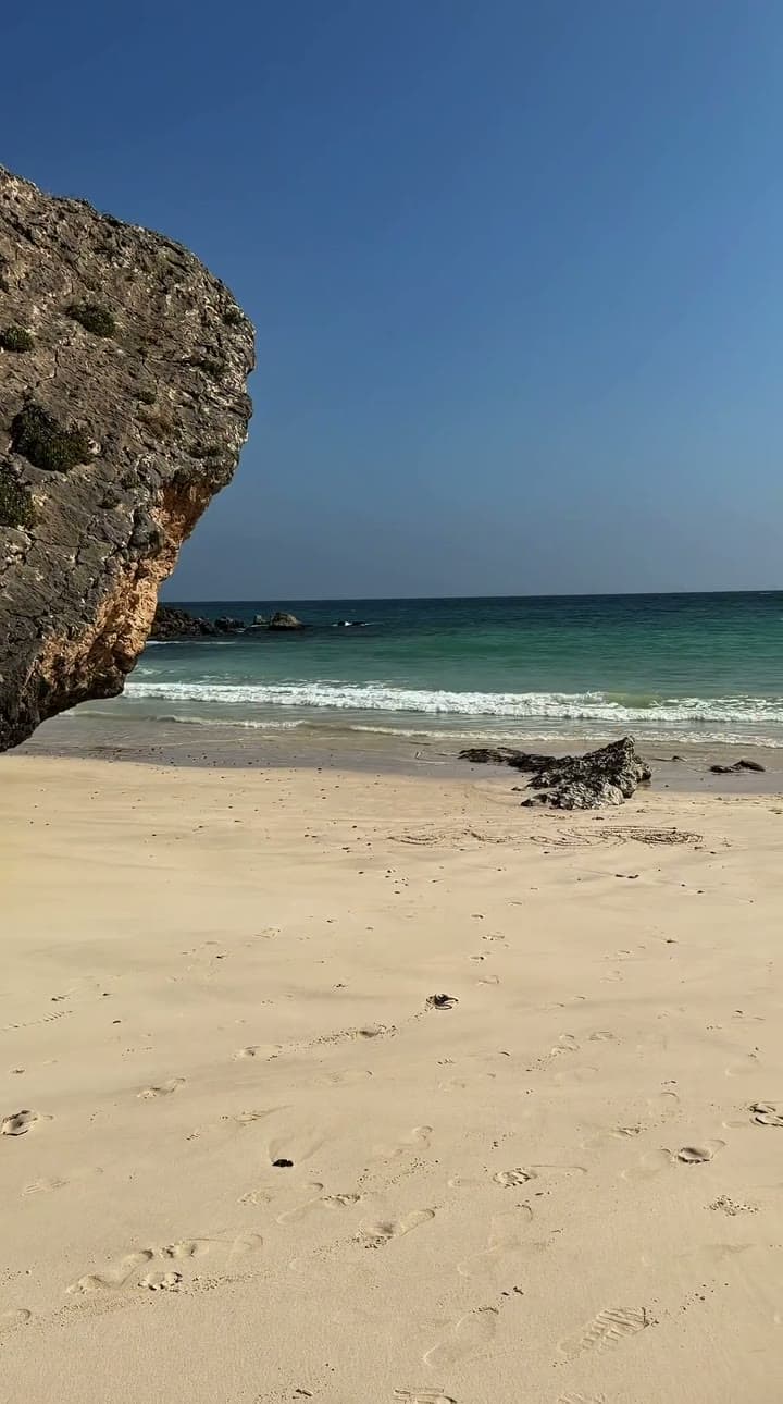 An overhanging limestone rock above an empty white beach and turquoise shallows