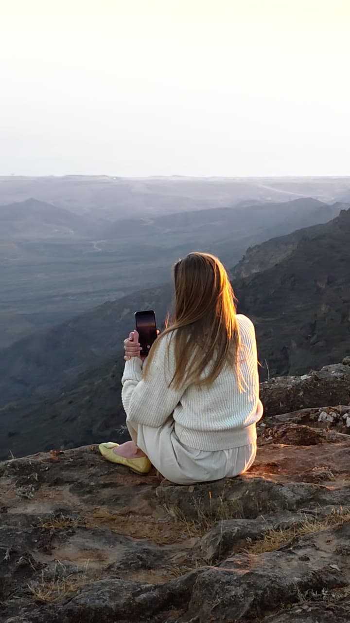 A woman sitting at the edge of a cliff above a hazy valley