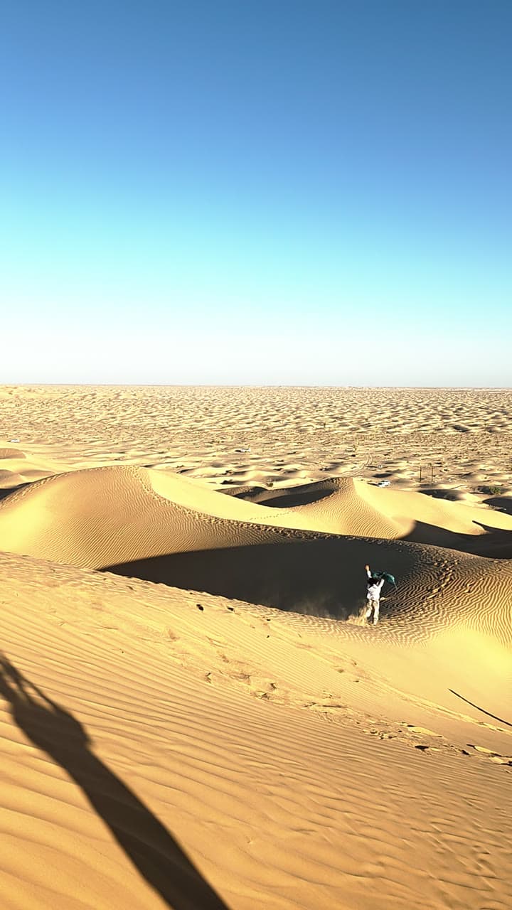 A single figure crossing a vast field of dunes, long shadows raking the sand