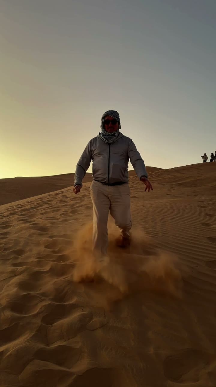 Walking down a steep dune into low sun, sand kicked up underfoot