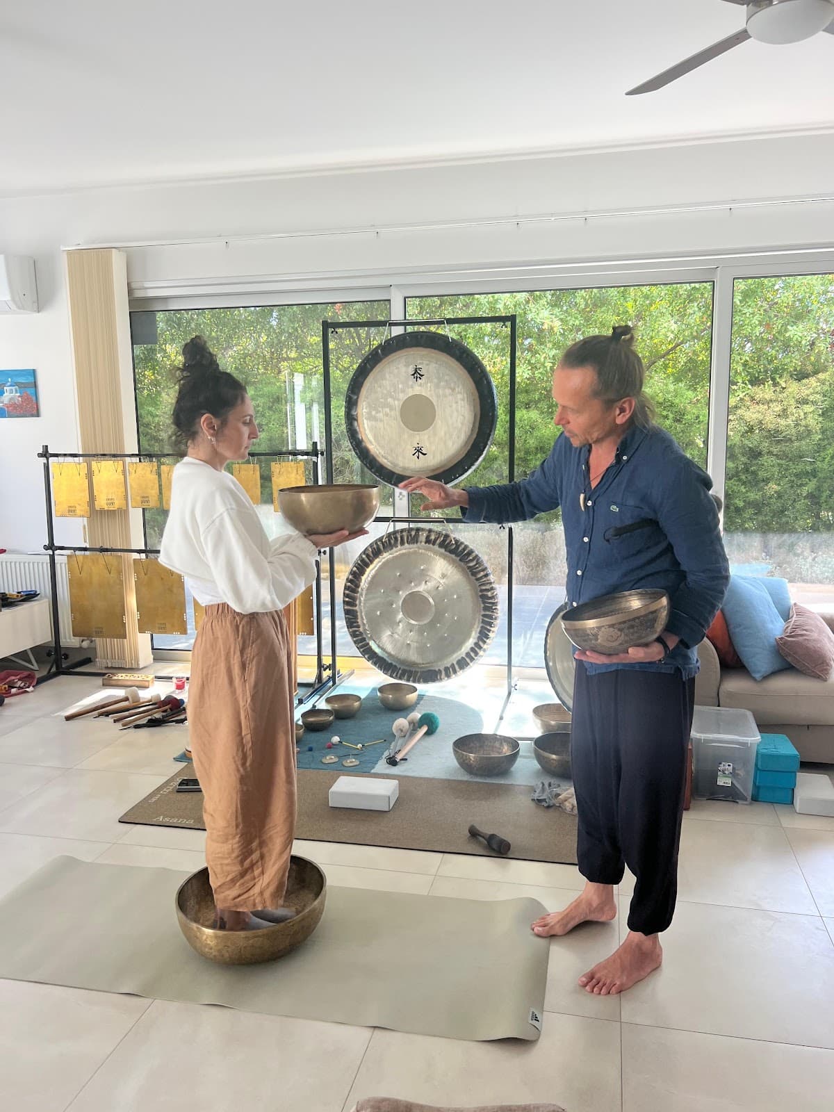 A singing bowl held over a participant standing in a second bowl, gongs hanging behind, a photo posted with Victoria Korelidou's review.