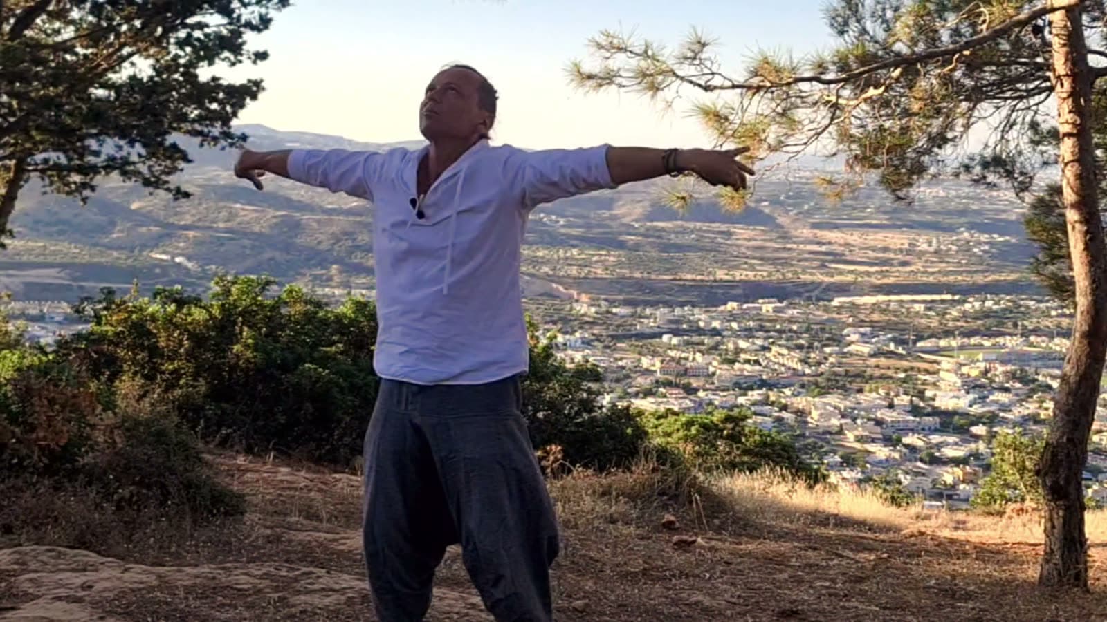 Morning practice with arms opened wide on a pine hillside above the valley